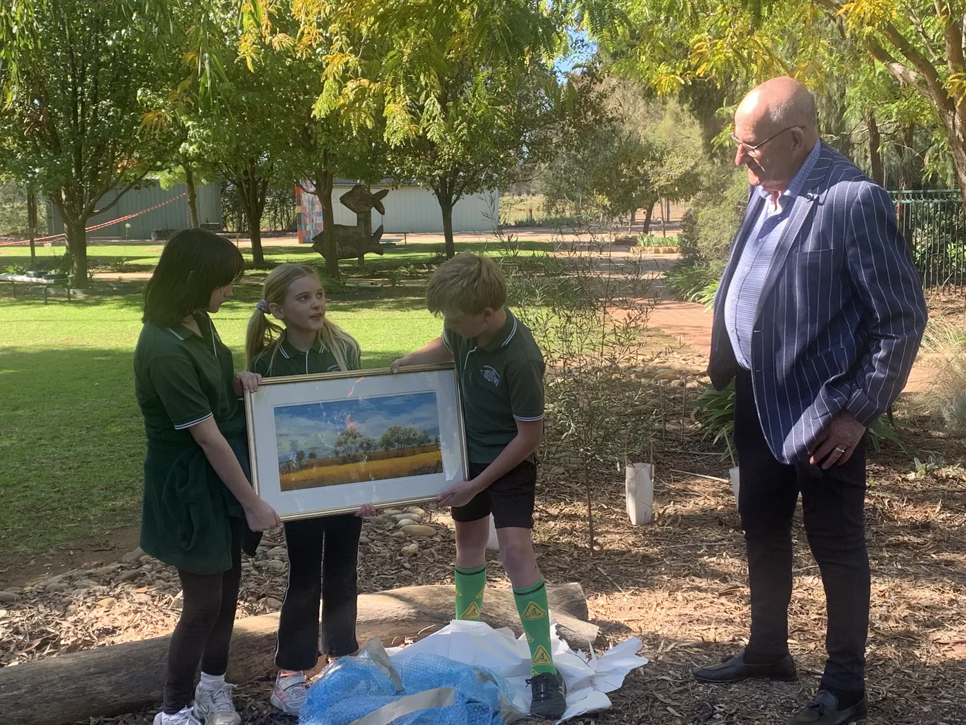 Carra students presenting a framed painting to a community member in the school grounds