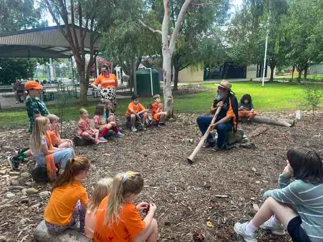 Uncle Dozer Atkinson playing the didgeridoo for a circle of Carra students in the native garden