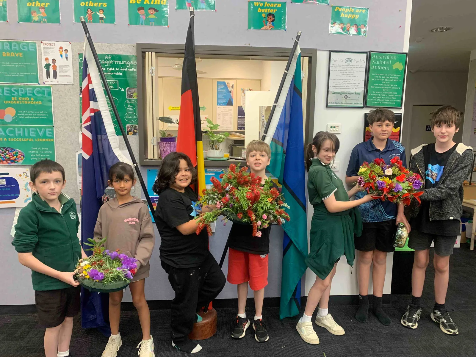 Carra students holding native flower arrangements they made, in front of the school flags