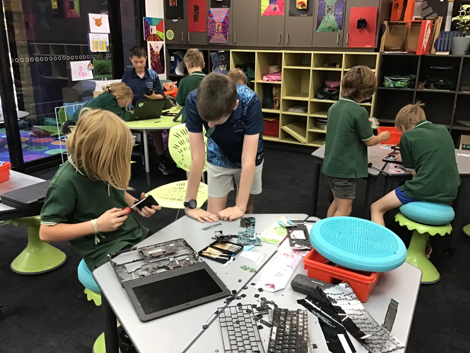 Carra students taking apart old laptops and keyboards at a table in a bright classroom