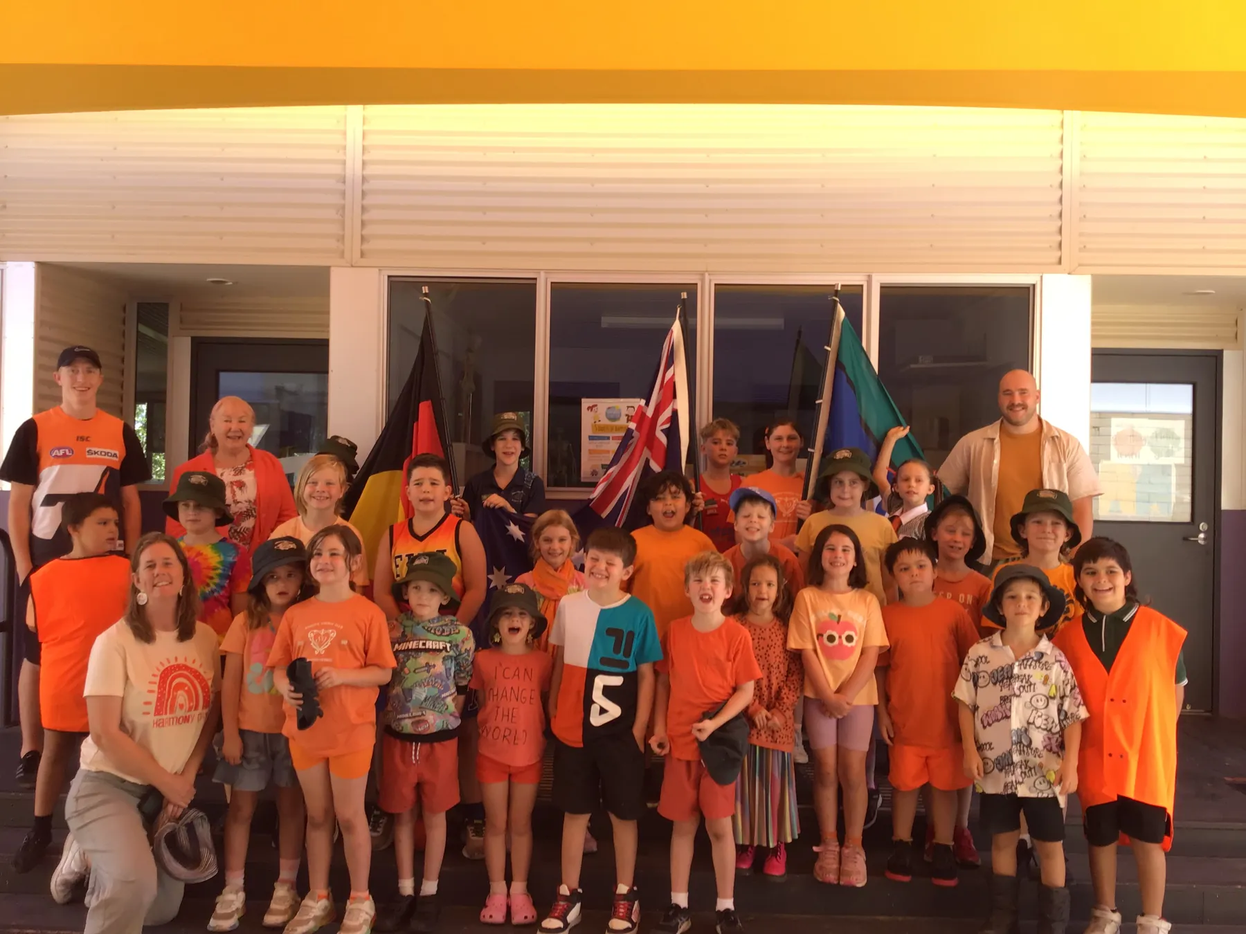 Carra students and staff in orange for Harmony Day, holding the Australian, Aboriginal and Torres Strait Islander flags