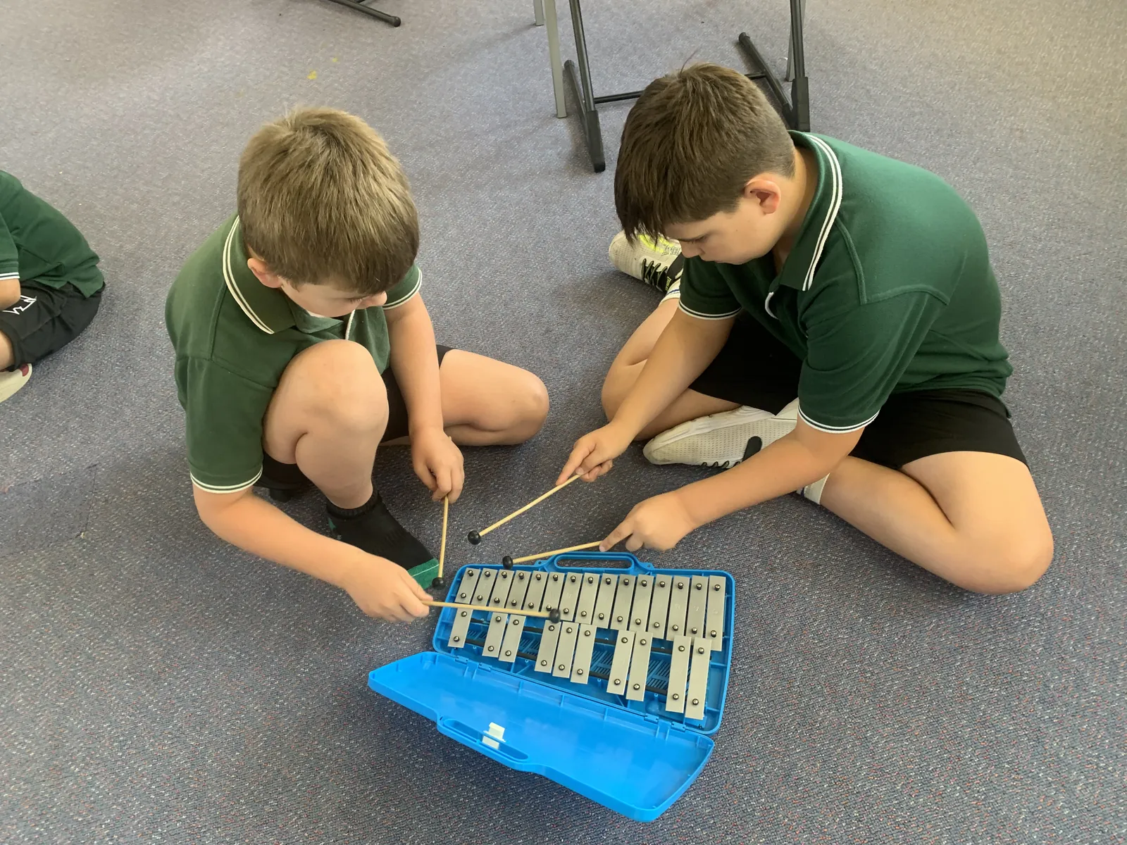 Two Carra students playing a glockenspiel together on the classroom floor
