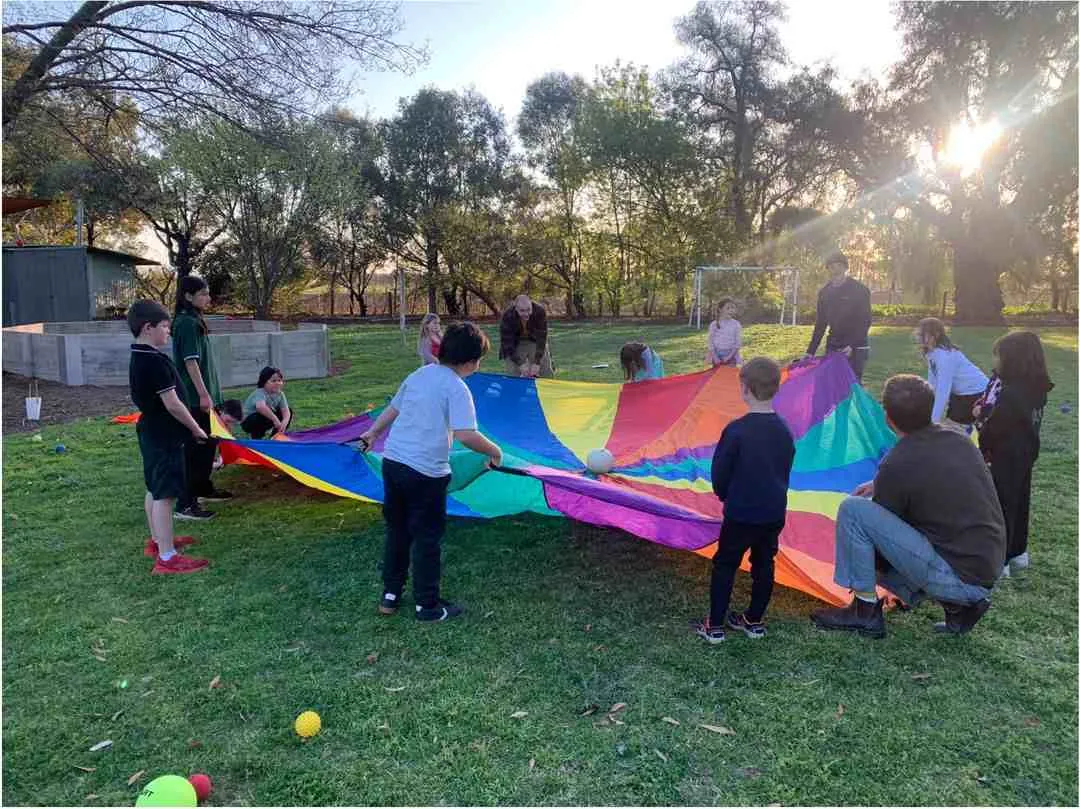 Carra students playing a group game with a rainbow parachute on the school grounds in the afternoon sun