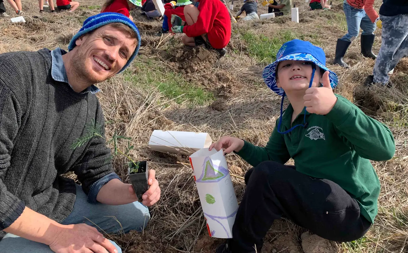 A teacher and a Carra student planting native tree seedlings together in a paddock