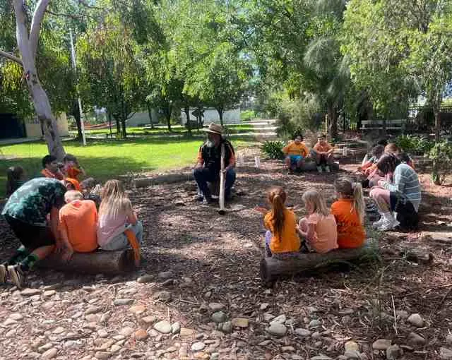 Carra students seated in a circle on logs in the native garden, listening to Uncle Dozer Atkinson
